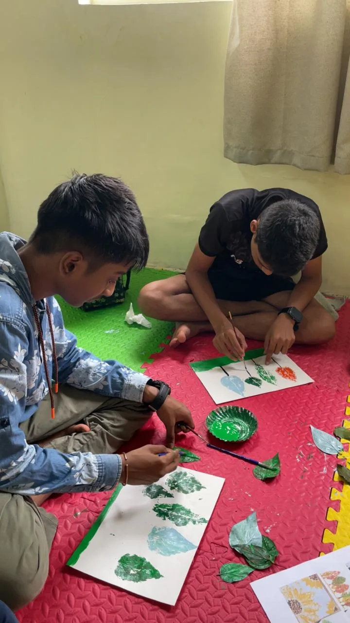 Two students making painted leaf prints on paper