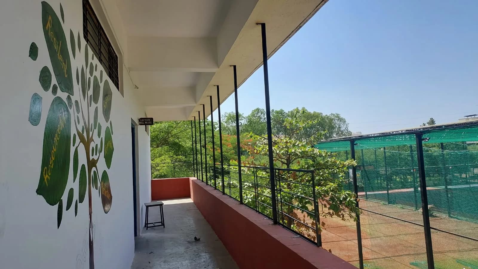 Open-air corridor with a painted values tree and a view of the sports area