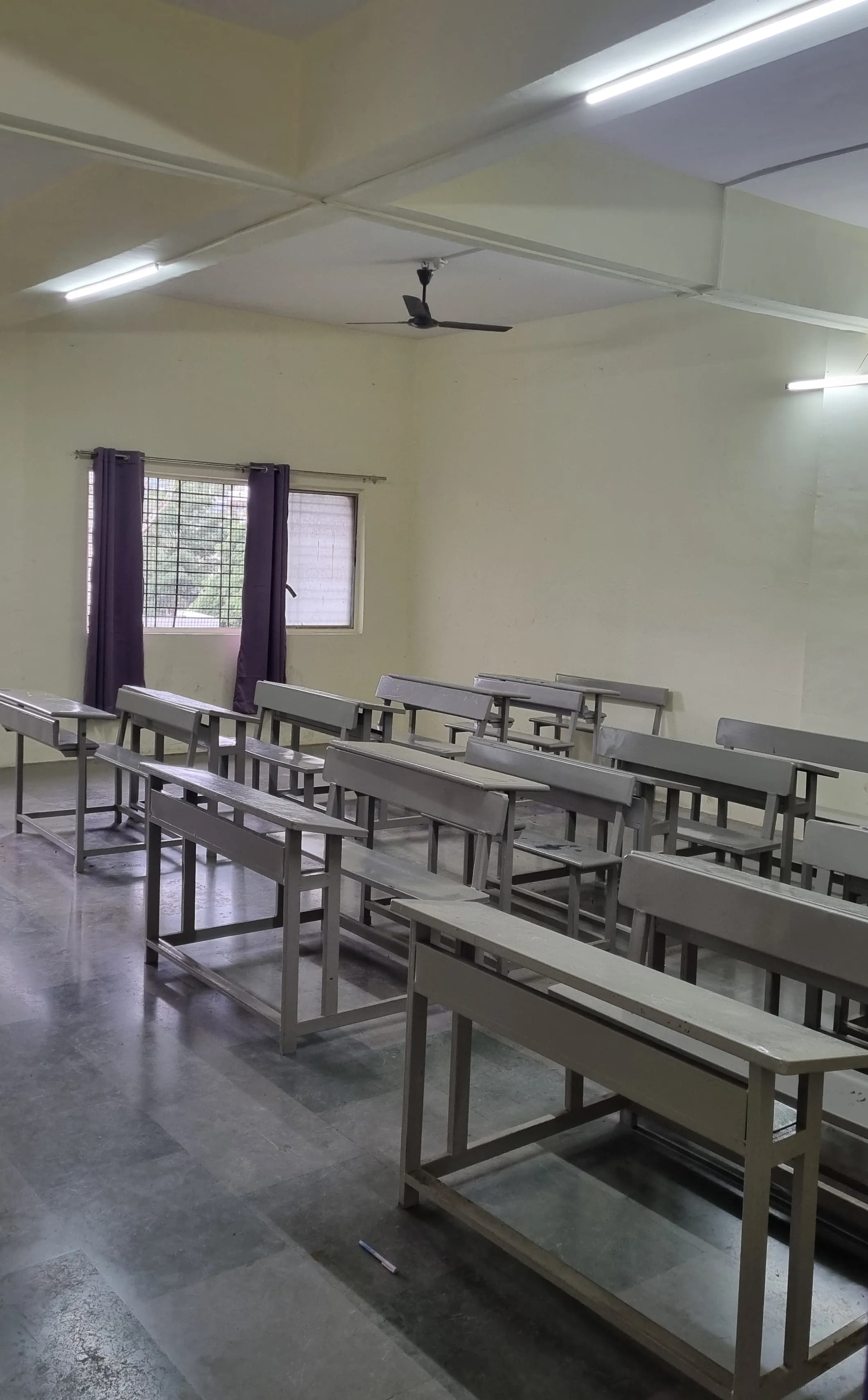 Rows of classroom benches beside a window with purple curtains